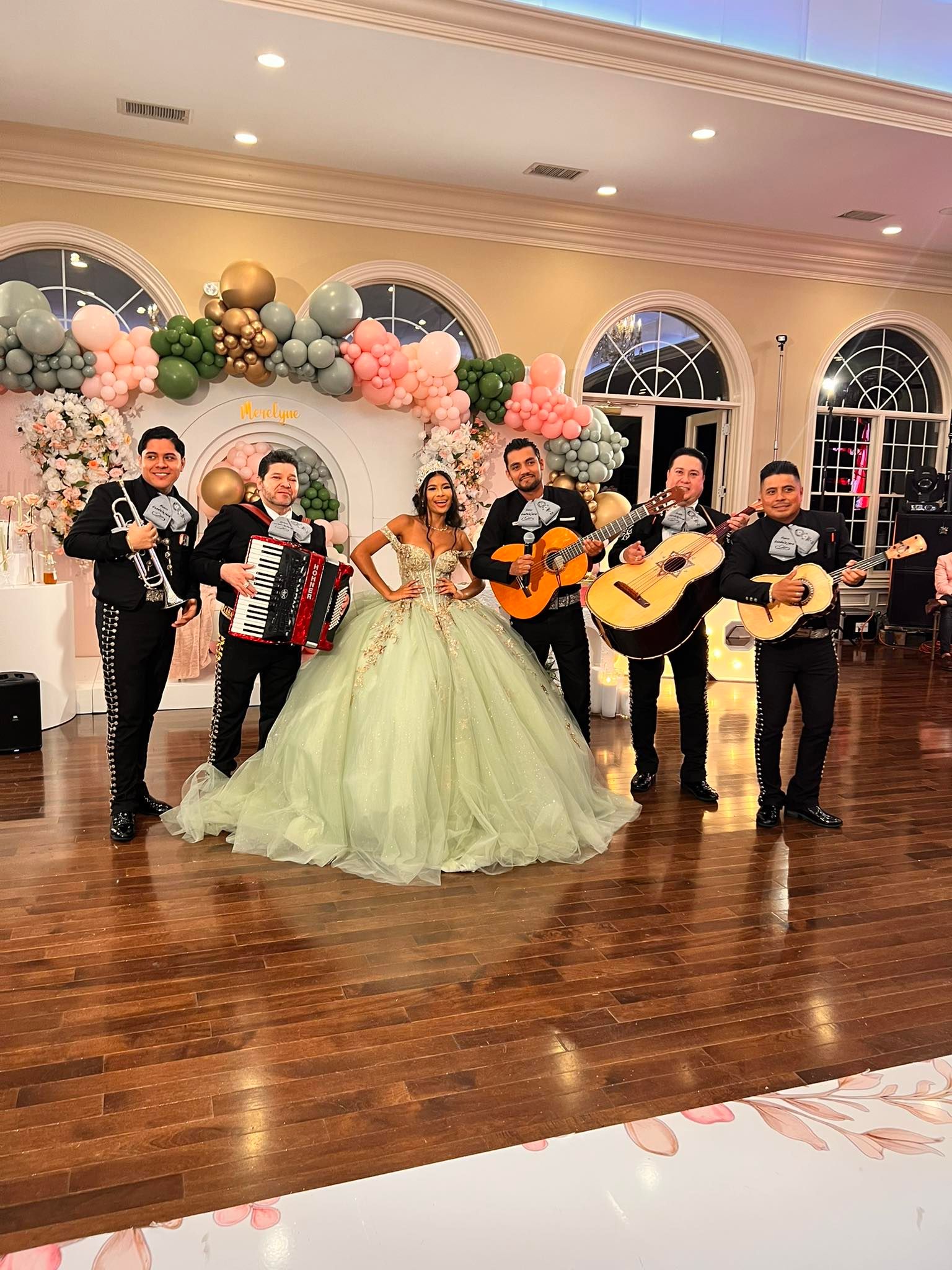 Mariachi y homenajeada en una fiesta con globos y flores.